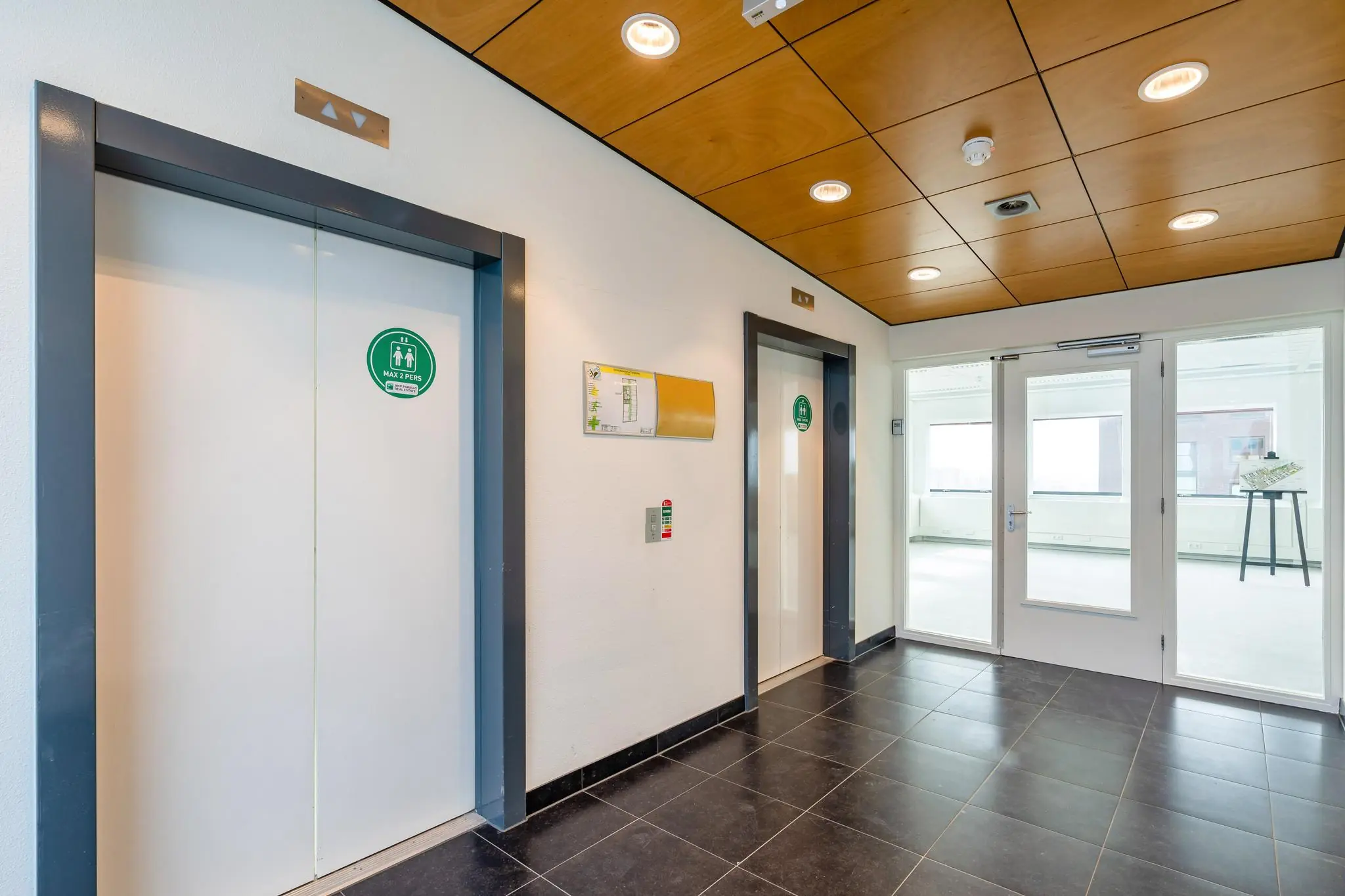 Liftlobby met twee liften en glazen toegangsdeuren in het Johanna Westerdijkplein-gebouw.